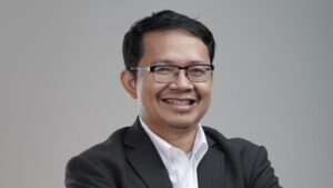 Pakar politik tersenyum mengenakan jas hitam membahas wacana koalisi permanen Bahlil dalam diskusi di studio